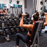 Woman exercising in the gym lifting dumbbells with headphones on for a strength-building workout.